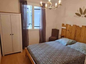 A bedroom with a bed, a wardrobe, a window with curtains, a wooden headboard, and a wall-mounted light fixture.