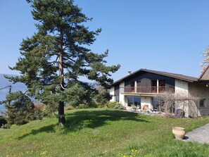 Ein zweistöckiges Haus mit Balkon, umgeben von einer Rasenfläche und Bäumen.