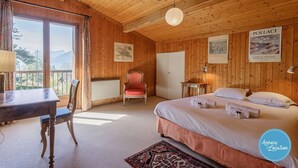 Een houten kamer met een bed, een stoel, een tafel en uitzicht op bergen.