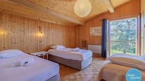 Een houten hutje met drie bedden, een houten plafond en een groot raam met uitzicht op bomen.