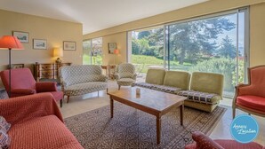 Een ruime woonkamer met een groot raam, een houten salontafel en diverse zitplaatsen, waaronder fauteuils en banken.
