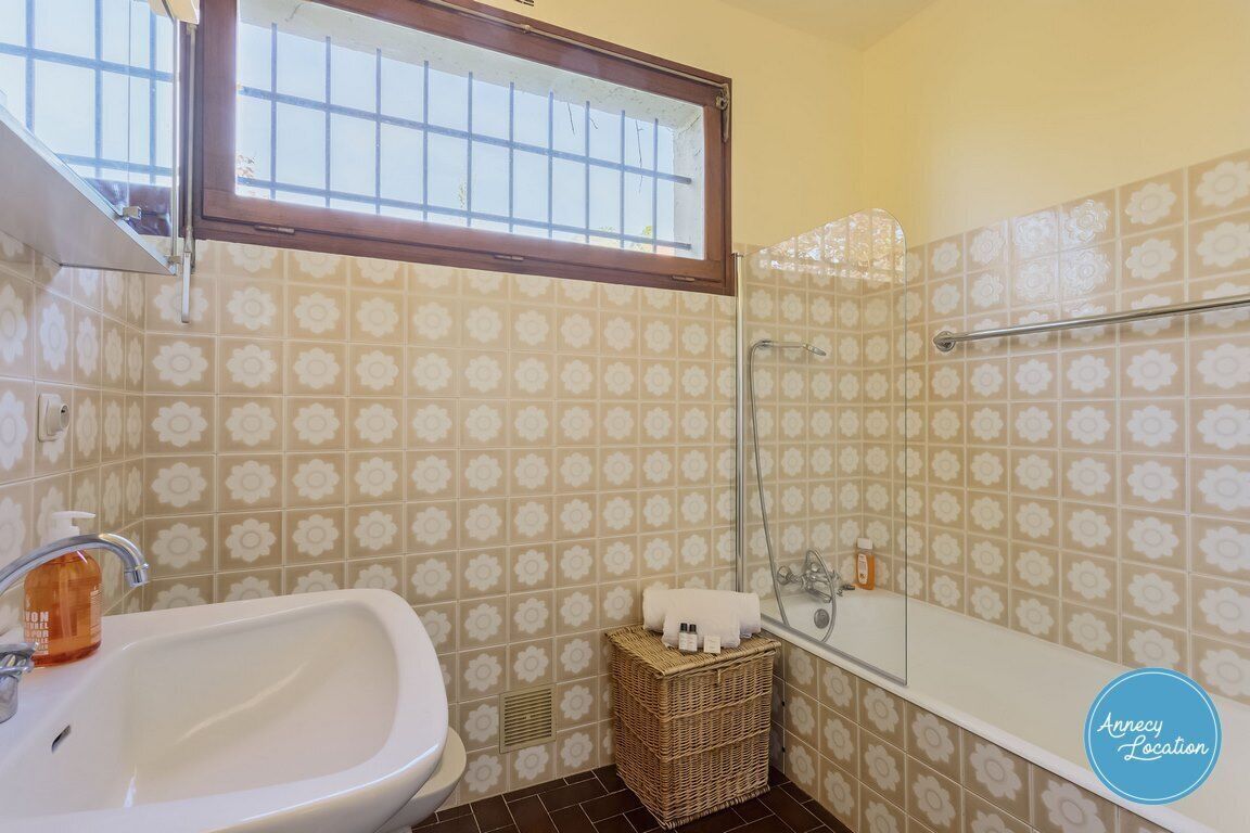 Un bagno con un lavandino bianco, una doccia e una finestra sopra il lavandino.