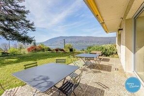 Eine Terrasse mit Tisch und Stühlen, Blick auf einen See und Berge in der Ferne.