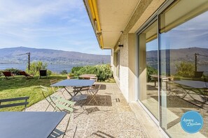 Eine Terrasse mit Gartenmöbeln, einer Glastür und Blick auf einen See und Berge.