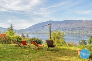 A view of a lake with mountains in the background, two lounge chairs, and a sign indicating 'Annecy Location'.
