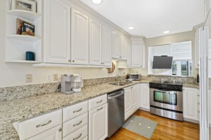 A modern kitchen with white cabinets, granite countertops, stainless steel appliances, and a built-in oven.