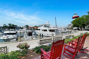 A marina with boats docked, a lighthouse in the background, and red chairs in the foreground.
