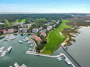 An aerial view of a marina with boats docked, a golf course, and surrounding buildings.