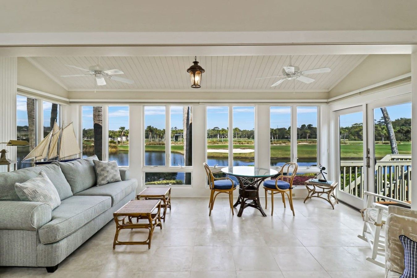 Ein geräumiges Zimmer mit großem Fenster und Blick auf einen Golfplatz, einem gemütlichen Sitzbereich mit Sofa und Sesseln sowie einem Deckenventilator.