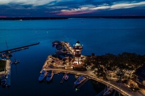 Ein Luftbild einer Marina mit vertäuten Booten, einem Leuchtturm und einer Pier, die sich ins Wasser erstreckt.