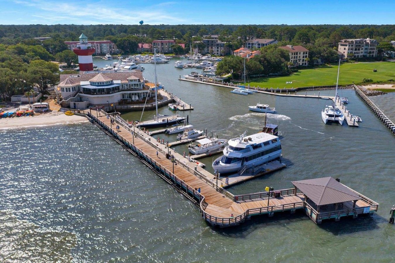 Un puerto deportivo con varias embarcaciones amarradas, un muelle que se adentra en el agua y edificios al fondo.
