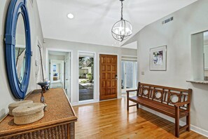 A spacious hallway with wooden flooring, a bench, a large mirror, and a door leading to a garden.