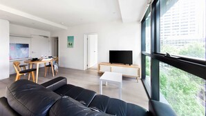 Ein modernes Wohnzimmer mit einer schwarzen Ledersofa, einem Essbereich mit einem Holztisch und einem Fernseher auf einem Schrank.