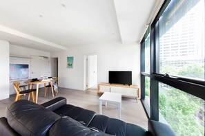 Un salon moderne avec un canapé en cuir noir, un coin repas doté d’une table en bois et un téléviseur posé sur un meuble.