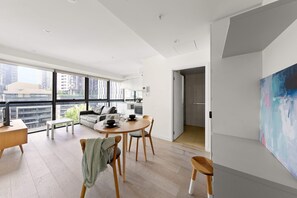 Un appartement moderne comprenant un coin repas, un salon avec un canapé et une table basse, ainsi qu’une grande fenêtre donnant sur la ville.