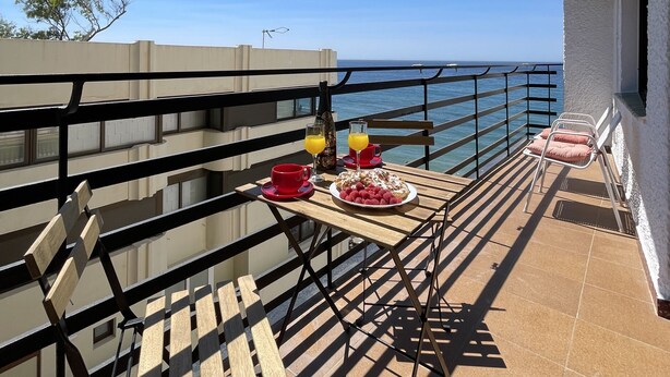 A balcony with a table set for breakfast, overlooking the sea.