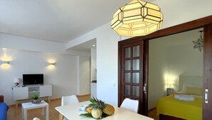 A modern hotel room with a dining area, a bed with a yellow bedspread, and a large window.
