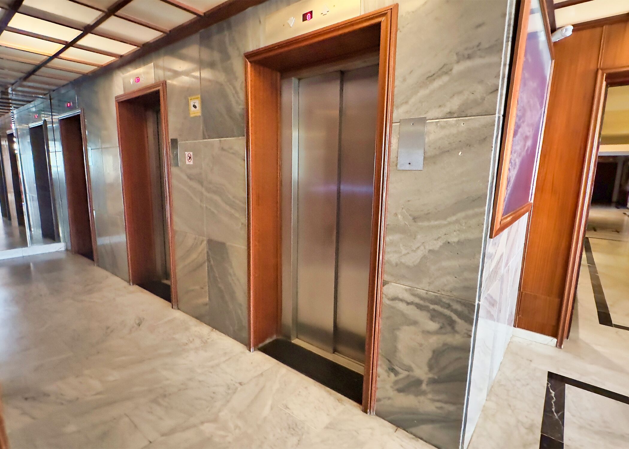 A hallway with marble flooring and wooden doors leading to elevators.