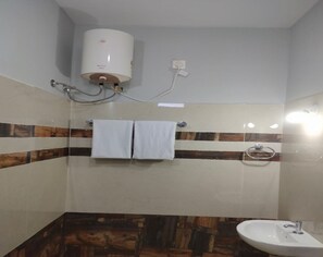 A bathroom with a white sink, a towel rack with two towels, a showerhead, and a water heater mounted on the wall. - JK Resort (Yercaud)