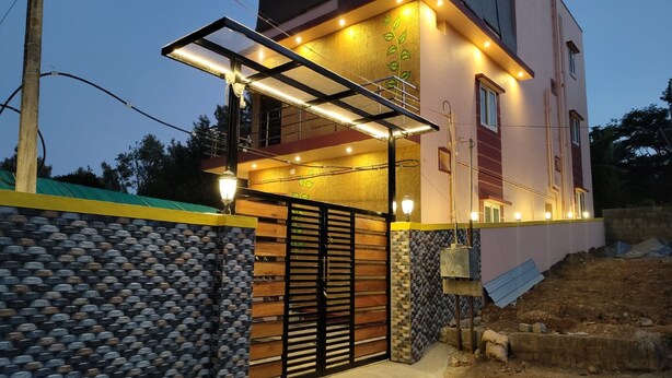 Una casa moderna de dos pisos con balcón de vidrio, entrada con portón y exterior bien iluminado.