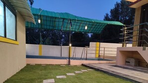 Un espacio exterior bien cuidado con césped verde, un sendero de piedra y una zona de estar cubierta con techo verde.