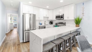 A modern kitchen with white cabinetry, stainless steel appliances, and a marble island with bar stools.