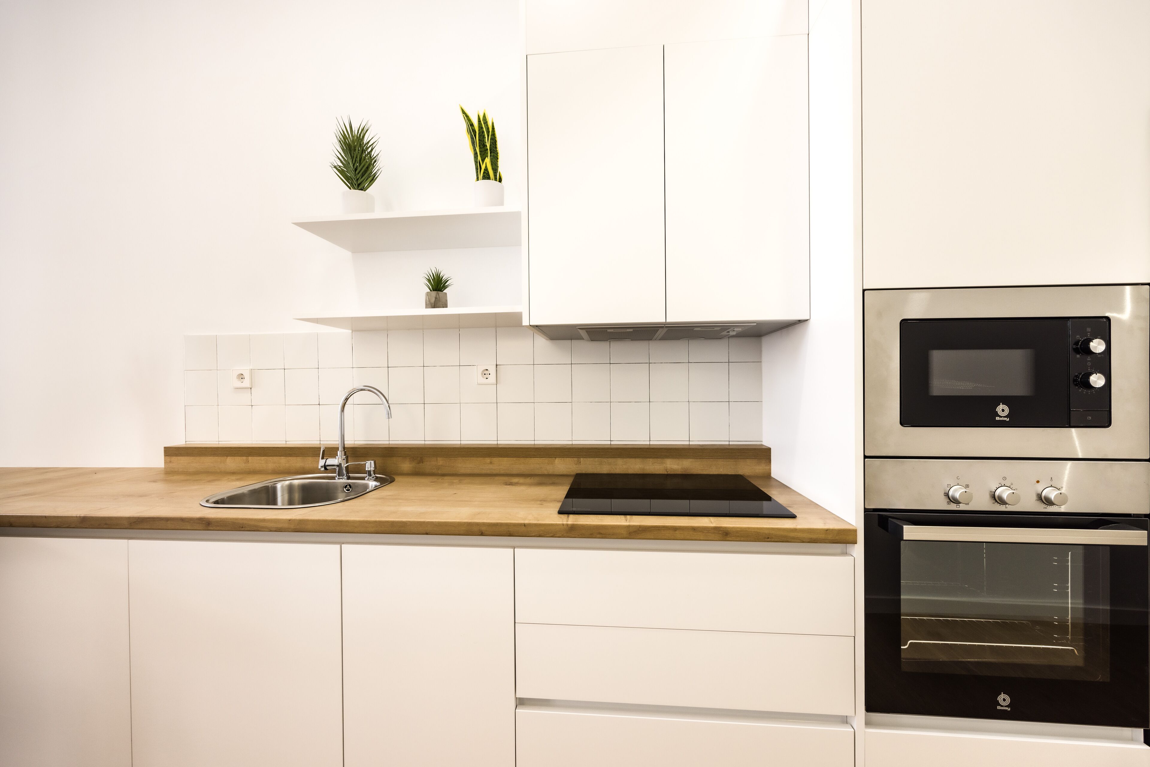 Una cocina moderna con armarios blancos, encimera de madera, pileta de acero inoxidable y horno empotrado.