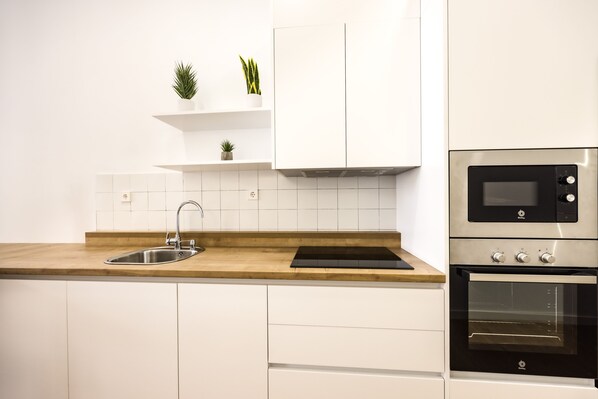 A modern kitchen with white cabinets, a wooden countertop, a stainless steel sink, and a built-in oven.