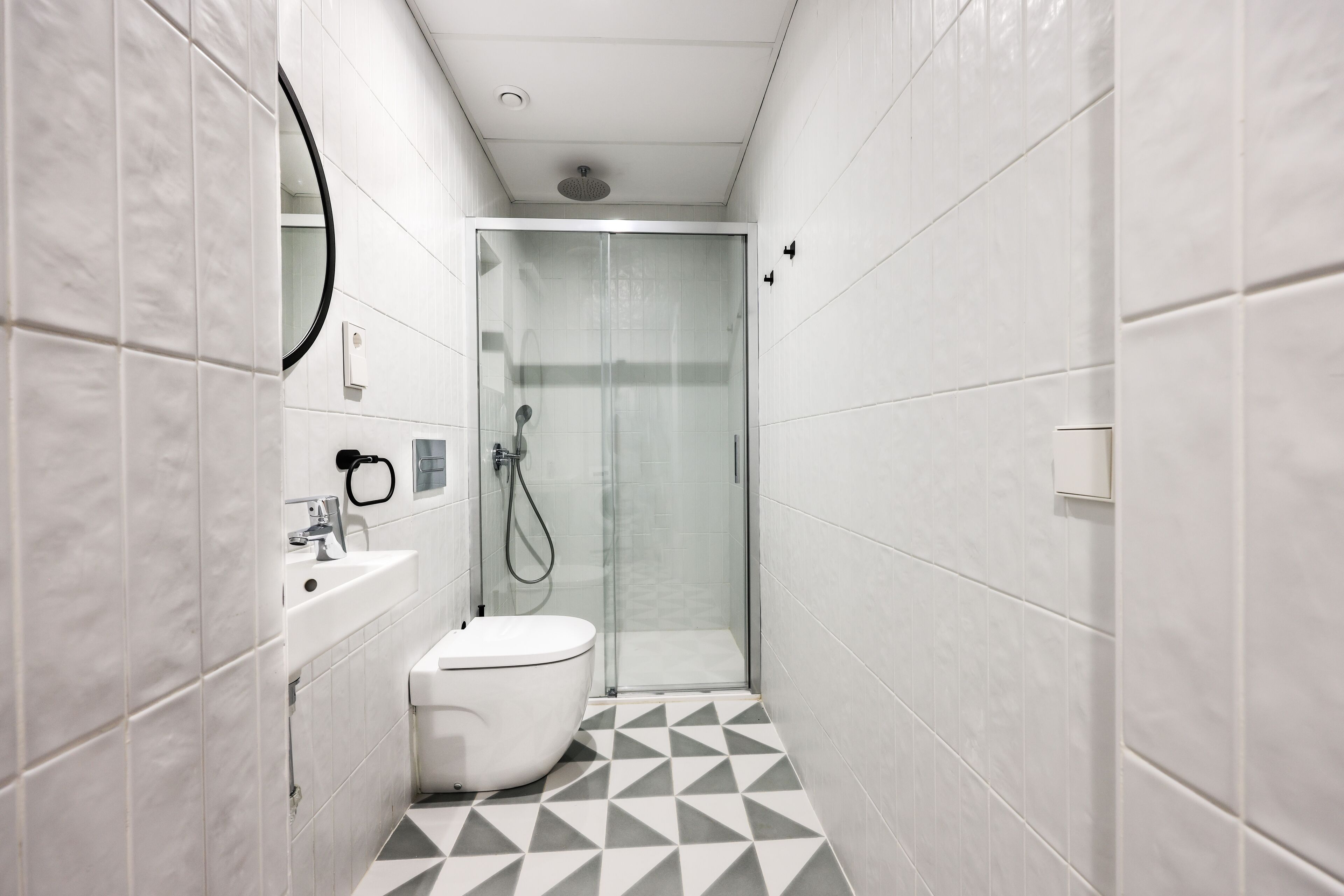 A narrow bathroom with a white toilet, a sink, and a glass-enclosed shower.