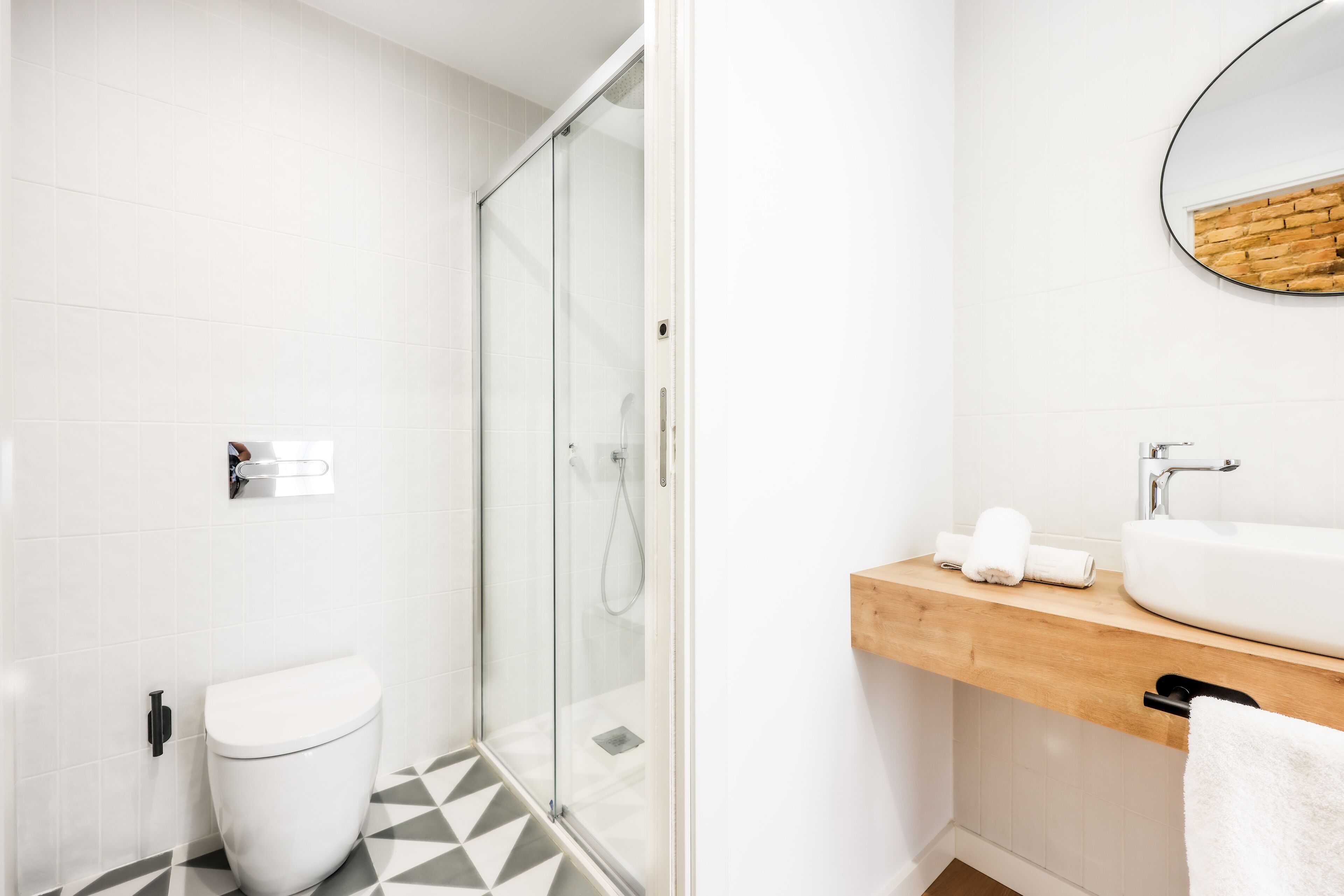 A modern bathroom with a glass shower enclosure, a white toilet, and a wooden vanity with a sink and towel rack.