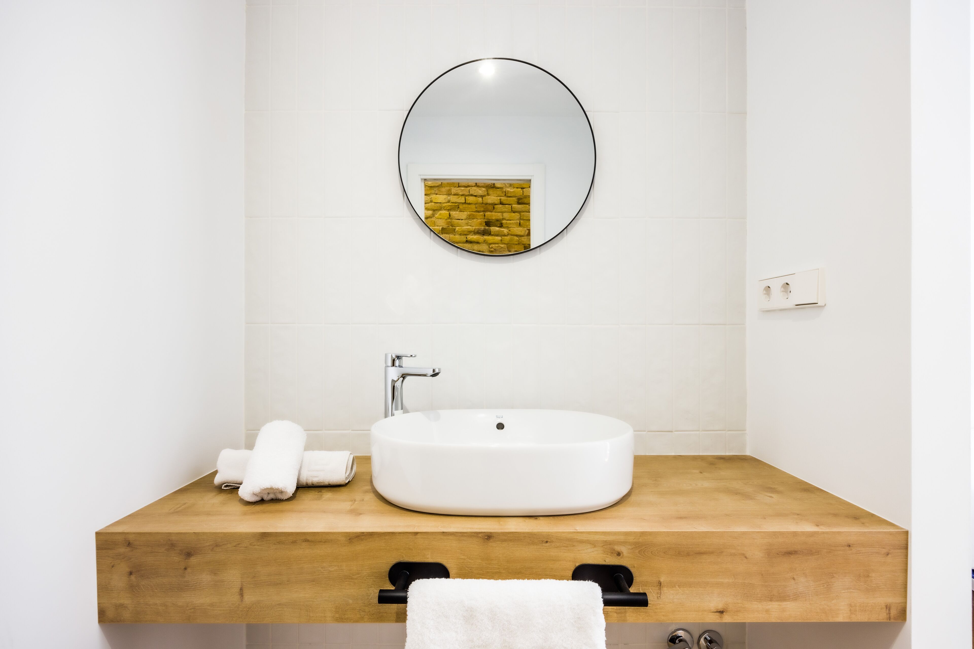 Een badkamer met een houten wastafelmeubel, een witte wasbak en een ronde spiegel.
