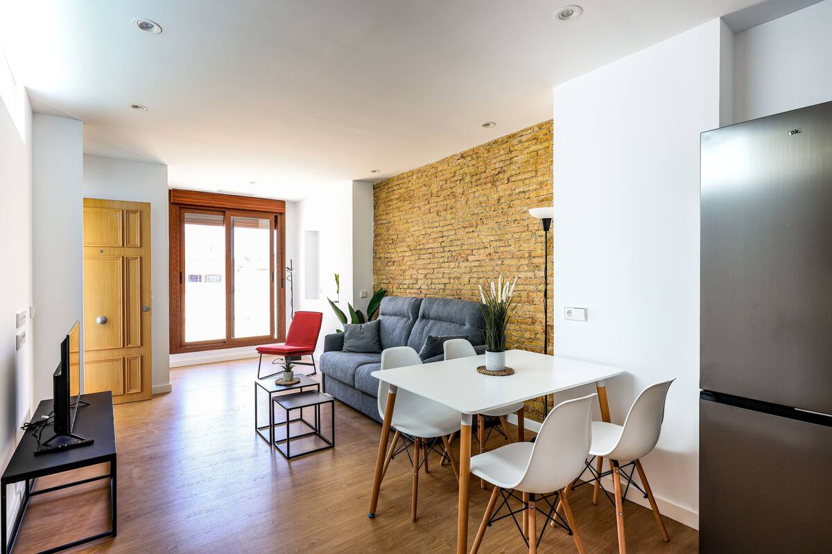 A modern living space with a dining area, a sofa, and a kitchen.