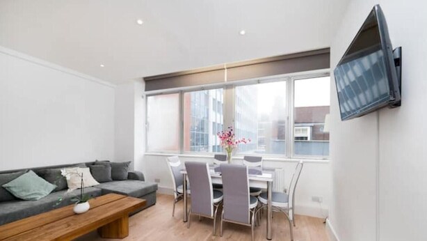 Una sala moderna con sofá, una mesa de centro, una mesa de comedor, sillas y un televisor montado en la pared.