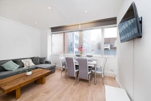A modern living room with a sofa, coffee table, dining table, chairs, and a TV mounted on the wall.