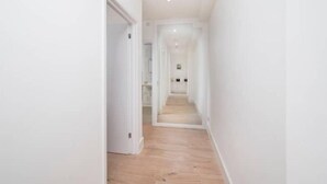 Un estrecho pasillo de tonos claros con suelo de madera que conduce a una habitación con paredes blancas y una puerta.