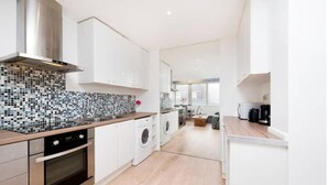 Una cocina moderna con armarios blancos, salpicadero de azulejos, campana extractora de acero inoxidable, horno integrado y lavadora.