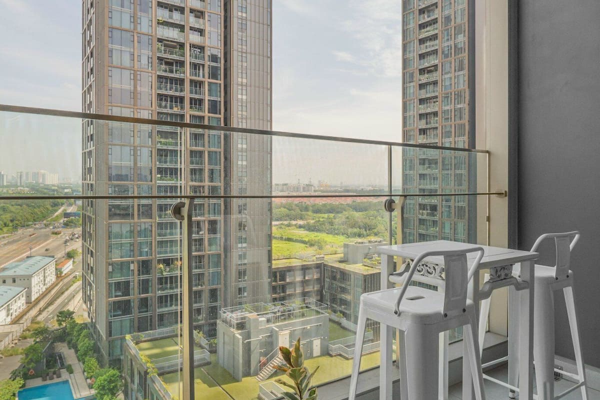 A balcony with a view of tall buildings, a glass railing, and potted plants.