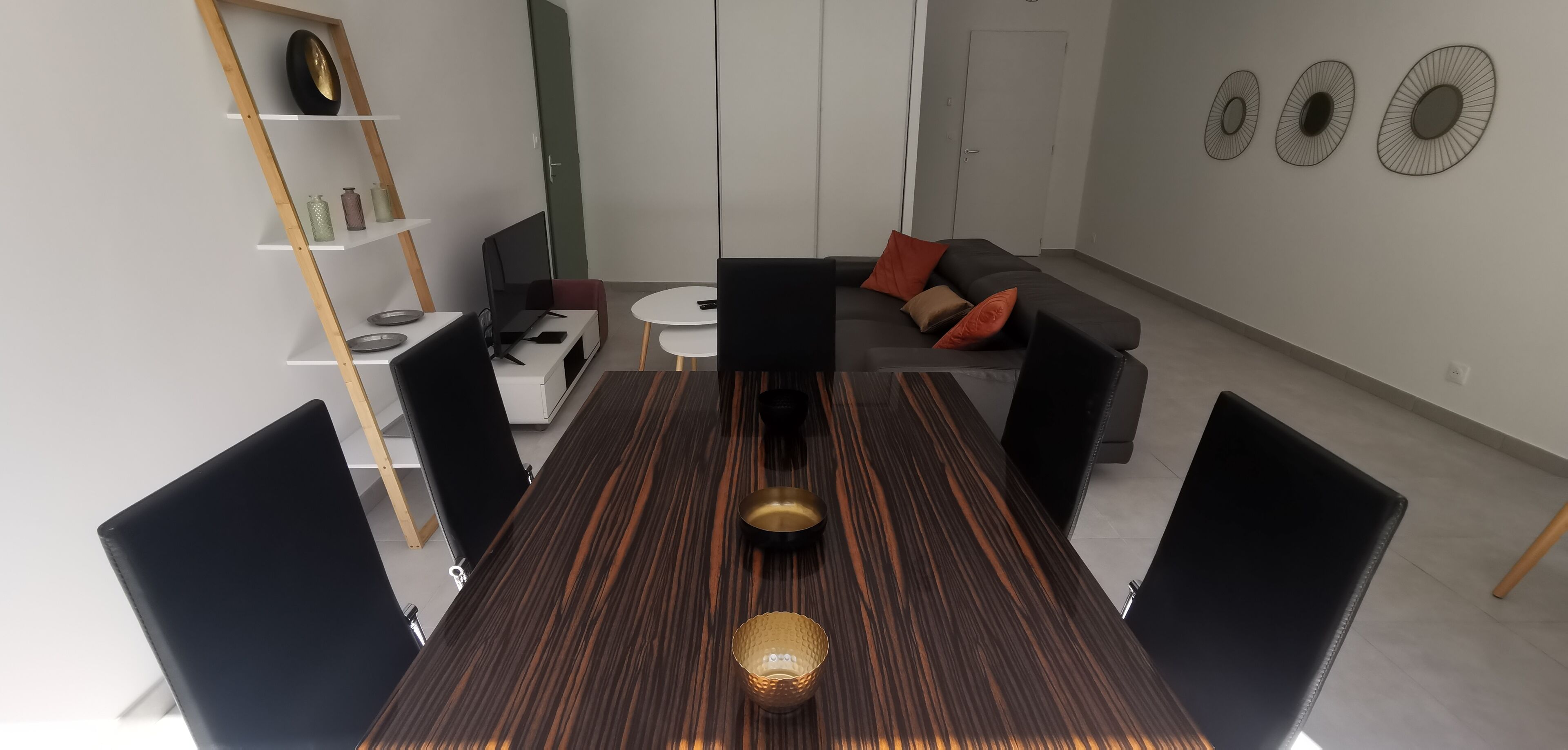 Een moderne woonkamer met een eettafel, zwarte stoelen, een bank met kussens, een boekenkast en decoratieve muurkunst.