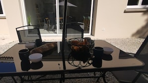 An outdoor table with a baguette, bowls, and cups, set against a building with a sliding glass door. - Nouvelle Villa Provençale Calme, Proche du Centre (Montélimar)