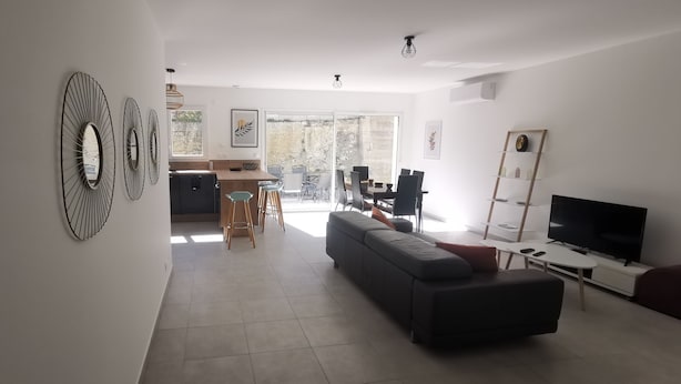 A modern living room with a black sectional sofa, a TV, and a dining area with chairs and a table. - Nouvelle Villa Provençale Calme, Proche du Centre (Montélimar)