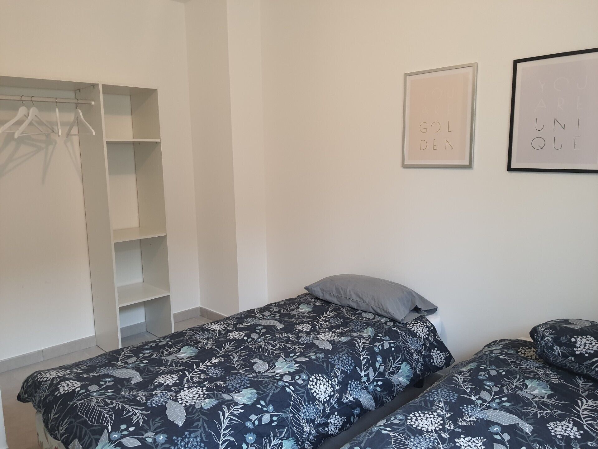 A bedroom with two beds, a wardrobe, and two framed motivational posters on the wall.