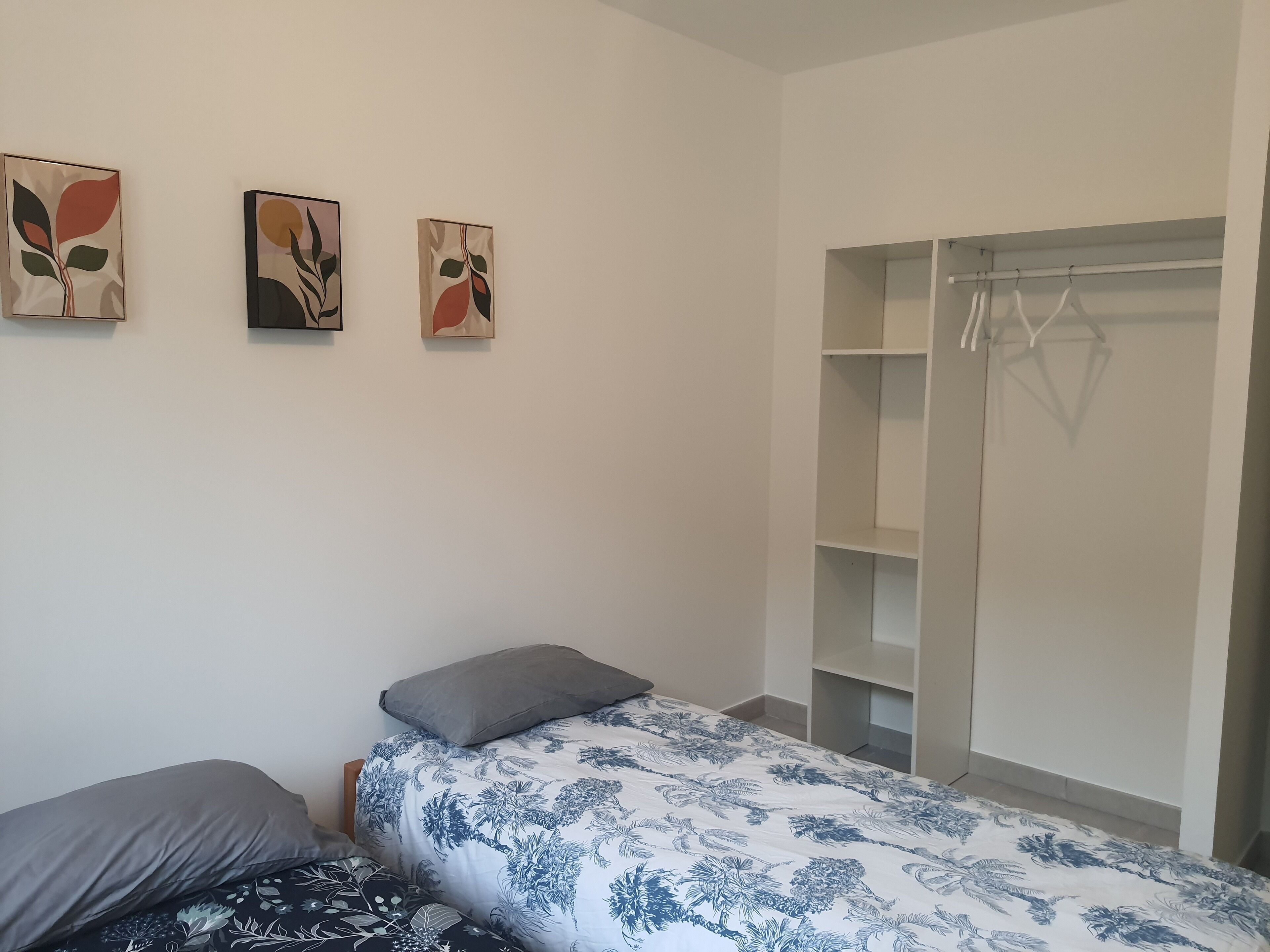 A bedroom with a bed, a grey pillow, a wardrobe, and three abstract wall art pieces.