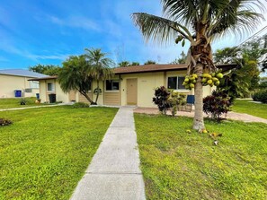 A single-story building with a front entrance, a pathway leading to the door, and a palm tree with coconuts. - Near Ft Myers Beach • 3mi to Sand • Sleeps 7 (Fort Myers Beach)