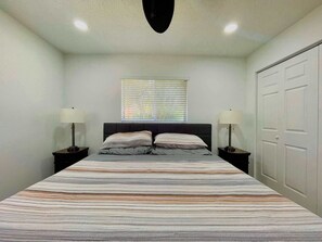 Ein Schlafzimmer mit einem Bett, zwei Nachttischen mit Lampen, einem Fenster mit Jalousien und einem Kleiderschrank.