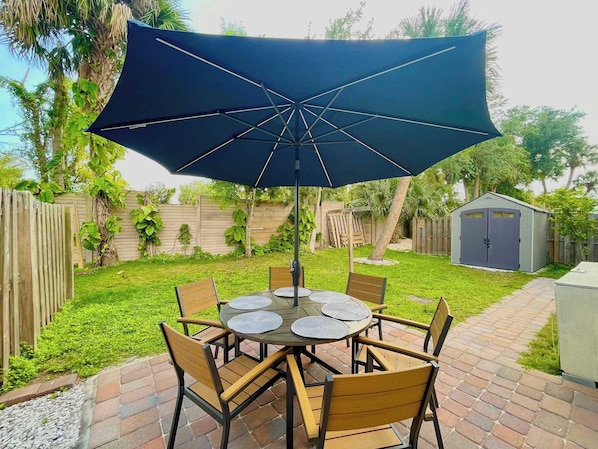 Eine Terrasse mit einem runden Tisch, sechs Stühlen und einem großen Sonnenschirm.