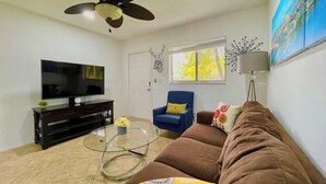 Ein Wohnzimmer mit Fernseher, Deckenventilator, Sofa, Couchtisch und einem Sessel.
