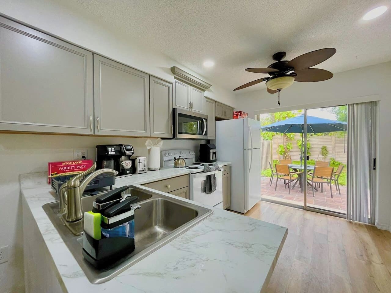 A modern kitchen with a central island, stainless steel appliances, and a sliding glass door leading to an outdoor patio.