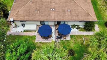 A two-story building with a tiled roof, a patio with two umbrellas, and a garden area with various plants.