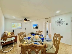 A dining area with a glass table, wooden chairs, and a ceiling fan.