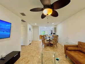 A modern living room with a TV, a ceiling fan, a dining area, and a sofa.